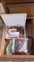 Open box showing insulated clip leads, Commercial Electric manual, yellow-handled wire stripper, multimeter in plastic bag, hex key