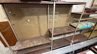 Front view of full shelving unit showing metal frame, wood shelves, pegboard back, some hooks
