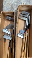 Two cardboard boxes holding antique golf irons