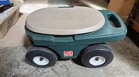 Top view showing beige lid, green body, four wheels and Step2 logo