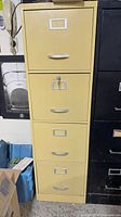 Front view of yellow four-drawer metal filing cabinet with label frames and handles, key in lock