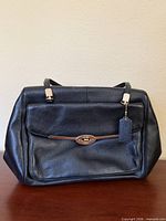 Front view of black Coach leather satchel showing flap pocket and handles