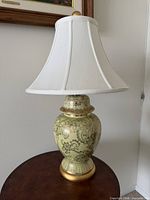 Full view of ceramic gold floral temple jar lamp with white bell shade on wooden table