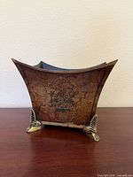 Front of square flared planter showing crackle finish, floral motif, and two gilt metal feet