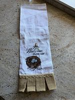 Full view of white embroidered tea towel with burlap hem