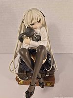 Front angle showing figure seated on suitcase hugging plush