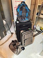 All four luggage pieces stacked: large black suitcase, smaller gray rolling suitcase, gray duffel, blue/gray backpack