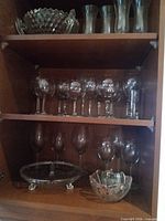 Overall view of three shelves showing assorted clear cut glass stemware, goblets, bowls and serving platter