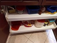 Overview of two cabinet pull-out shelves showing assorted storage containers, pepper mill, basket, lids and plate