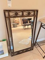 Full view of rectangular bronze and gold leaf decorative mirror leaning against wall