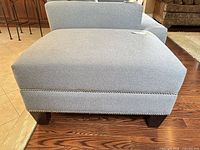 Full side view of ottoman showing overall shape, upholstery, nailhead trim and legs