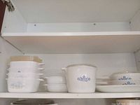 Full shelf view showing stacked casseroles, lids, ramekins, Blue Cornflower casserole, oval bakers and platter