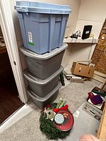 Stack of four plastic storage totes with holiday items at base