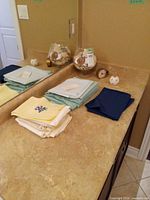Stacked pastel and navy linens, glass shell bowl, small clock, potpourri orb on countertop