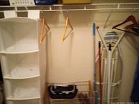 Closet view showing fabric organizer, wooden hangers, wire basket and portion of ironing board