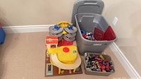 Overall lot showing Fisher-Price garage, spiral track, gray tote, beige bin with cars