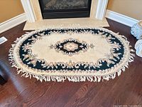 Full view of oval cream and green floral wool rug in front of fireplace with fringe