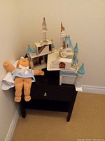 Overall view of white and blue plastic castle on small table beside baby doll in blue outfit