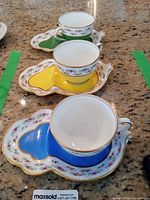 Three coloured teacup and saucer sets on countertop