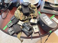 Overall lot view showing cameras, binoculars, cases, chargers and bags