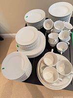 Multiple stacks of white embossed plates, cups and saucers on table