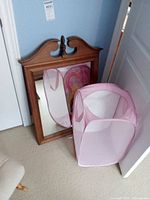 Wood framed mirror with pink pop-up hamper in front