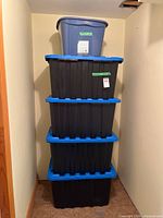 Stack of four black totes with blue lids and one grey bin on top