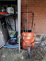 cabinet area with wheelbarrow front, shovels, rakes, sprayer, seed bag, bird feeder visible