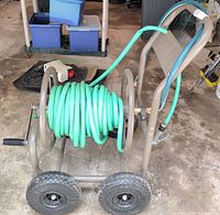 Side view of metal hose cart showing green hose wound on reel, pneumatic wheels, crank handle