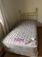 Full view of twin mattress on box spring with brass headboard and frame