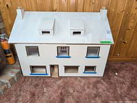 Front view of white-primed two-story plywood dollhouse with roof dormers and chimneys