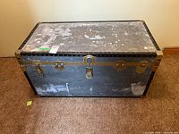 Front view of metal steamer trunk showing brass hardware and wear