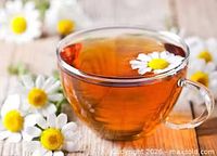 Cup of chamomile tea on wooden surface with daisies
