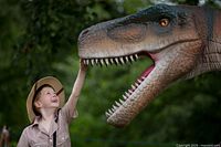 Child reaching toward life-sized animatronic dinosaur head