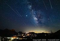 Starry sky with multiple meteor streaks over landscape