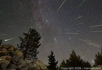 Meteor shower streaks across night sky over forested landscape