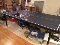 Full view of assembled blue table tennis table in a room with boxes