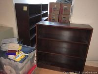 Three wooden bookcases seen together with some plastic bins and cardboard boxes nearby.