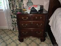 Front view of a dark brown wood nightstand with four drawers and brass-tone handles.