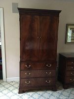 Front view of the hardwood armoire showing two doors above three drawers with brass handles and knob hardware, decorative crown molding, and wood grain finish.