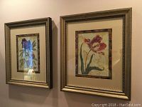 Two gold-toned framed floral prints with beaded trim and multicolor inner borders hanging on a wall.