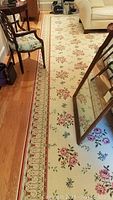 View of the rug laid out on hardwood floor with furniture surrounding it, displaying the floral pattern and decorative border.