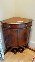 Front angled view of quarter circle corner cabinet table showing wood veneer finish, drawer, doors and brass hardware.