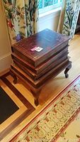 Closed book-shaped storage box on wooden stand with visible gold tooling and cabriole legs.