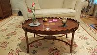 Front view of oval wooden coffee table with removable tray top showing decorative items on top.
