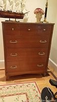 Front view of wooden dresser with four drawers and gold handles, showing three small top drawers with round knobs and two larger bottom drawers with horizontal handles.
