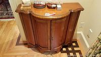 Front view of wooden sideboard with rounded cabinet and items placed on top, showing overall condition and design.