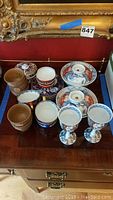 Full view of Japanese tea set and rice bowls arranged on wooden surface showing various cups, saucers, and bowls with lids