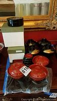 Overview of red lacquer covered bowls, stacked black lacquer bowls, and boxes.