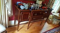 Wood buffet with gold handles and back rail, shown from the front and side angles, surface holds various dishware items.
